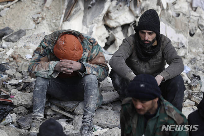 [알레포=AP/뉴시스] 7일(현지시간) 시리아 알레포에서 주민들이 지진으로 무너진 건물 잔해에 암울한 표정으로 앉아 있다. 튀르키예와 시리아를 강타한 지진으로 지금까지 사망자가 7800명을 넘은 것으로 나타났다. 2023.02.08.