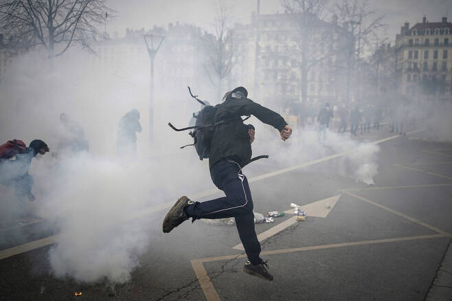 프랑스 연금개혁 반대 시위자가 23일(현지시각) 프랑스 리옹에서 시위를 진압하는 경찰들을 향해 돌을 던지고 있다. 툴레즈/AP 연합뉴스