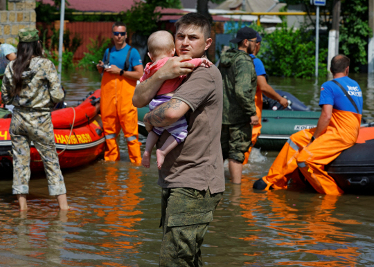러시아와 우크라이나가 지난 6일(현지시간) 발생한 우크라이나 남부 헤르손주의 카호우카 댐 폭발 사건의 배후에 대해 공방을 벌이고 있는 가운데 8일 한 남성이 댐 폭발로 침수된 헤르손주의 한 마을에서 아기를 안고 있다. 로이터·연합뉴스