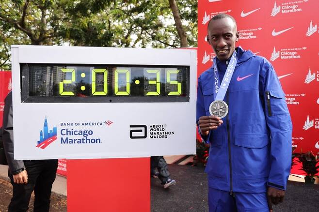 케냐의 켈빈 키프텀이 8일 시카고 마라톤에서 2시간00분35초의 세계신기록을 세우며 우승한 뒤 자신의 기록이 찍힌 전광판 앞에서 메달을 목에 걸고 포즈를 취하고 있다. AFP연합뉴스