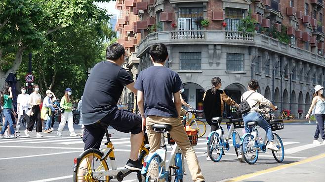 21일 중국 상하이 옛 프랑스 조계지의 랜드마크인 우캉빌딩 앞에서 자전거를 탄 청년들이 도로 위를 지나가고 있다. 일부 주거지역의 봉쇄가 먼저 풀리면서 상하이 거리에는 다시 시민들의 모습이 보이기 시작하고 있다. /연합뉴스