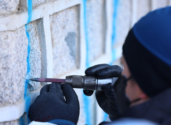 A preservation specialist tries to scrape off the paint carefully from the vandalized wall at Gyeongbok Palace on Saturday. Gyeongbok Palace is a state-designated historical site. [YONHAP]