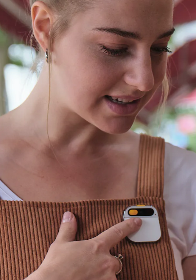 AI Pin을 웃옷 정면에 부착하고, 손으로 갖다 댄 다음 대화를 시작하는 사용자 /휴메인