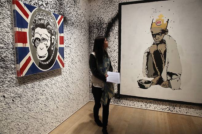 2014년 6월 영국 런던에서 열린 뱅크시 전시회에서 관람객이 작품을 관람하고 있다. 왼쪽 그림이 2003년작 ‘원숭이 여왕(Monkey Queen)’. 게티이미지