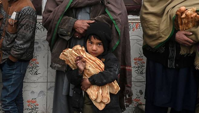 2022년 1월 18일 카불의 빵집 앞에서 한 아이가 구호단체가 무료로 나눠주는 빵을 받아들고 서있다. / AFP 연합뉴스