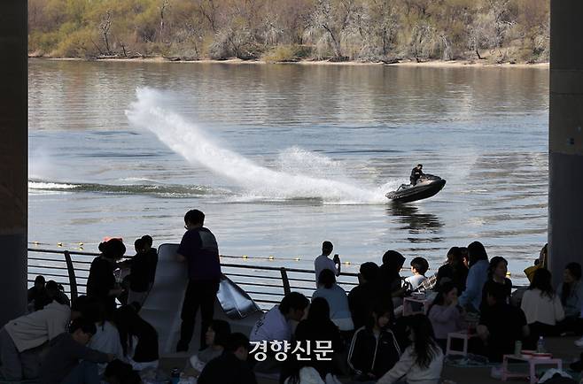 포근한 봄 날씨가 이어진 24일 서울 여의도한강공원을 찾은 시민들이 마포대교 밑에서 햇볕을 피하며 질주하는 제트스키를 바라보고 있다.