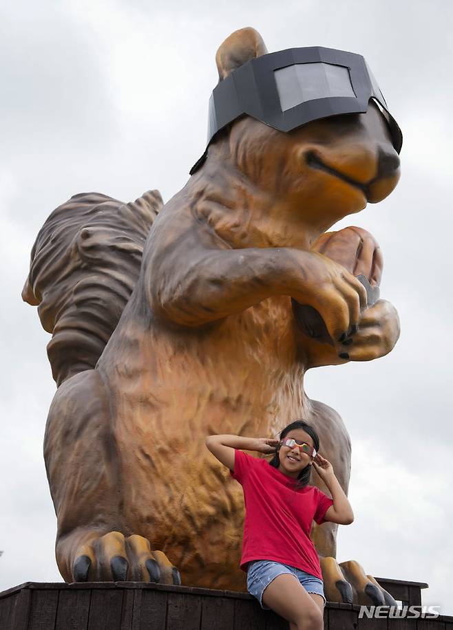 [시더크리크=AP/뉴시스] 8일(현지시각) 미 텍사스주 시더 크리크에서 관측경을 쓴 한 소녀가 대형 관측경을 쓴 다람쥐 동상 앞에서 개기일식을 기다리며 포즈를 취하고 있다. 2024.04.09.