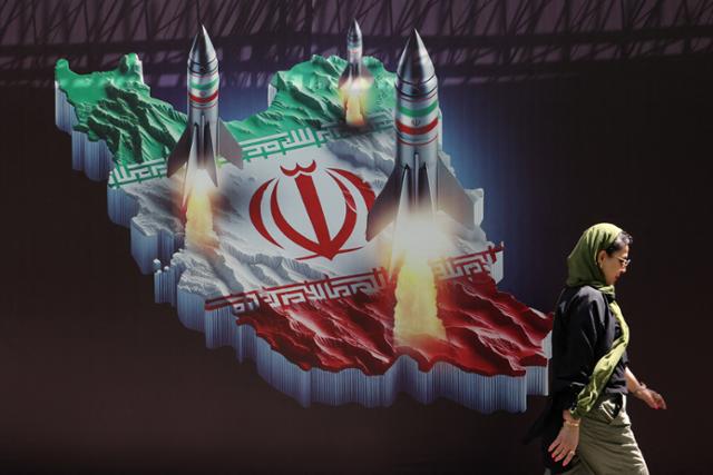 한 이란 여성이 19일 수도 테헤란의 한 거리에서 이란 국기와 미사일이 그려진 '반(反)이스라엘' 현수막 앞을 지나가고 있다. 테헤란=로이터 연합뉴스