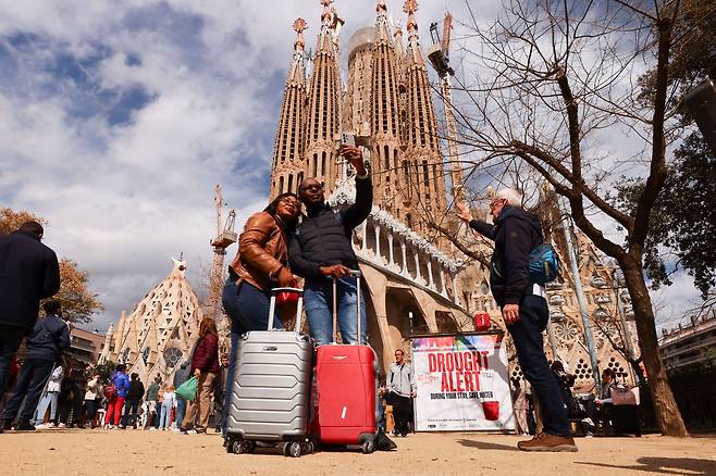 카탈루냐 정부가 바르셀로나를 포함한 200개 도시에 2월 초부터 가뭄 비상 상태를 선포한 가운데 물을 절약할 것을 촉구하는 사그라다 파밀리아 대성당 앞 표지판 옆에서 사진을 찍고 있는 관광객. / 로이터