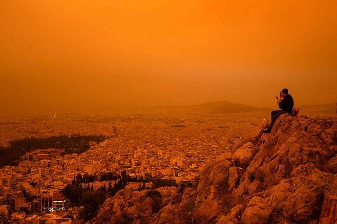 23일(현지시각) 그리스 아테네의 한 언덕에 사람들이 앉아 있고, 모래 폭풍의 영향으로 도시 일대가 주황빛으로 보인다. AFP 연합뉴스