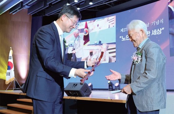 이기일 보건복지부 1차관(왼쪽)이 ‘제27회 노인의 날 기념식’에서 100세를 맞은 김택수 어르신께 청려장(장수지팡이)을 선물하고 있다.