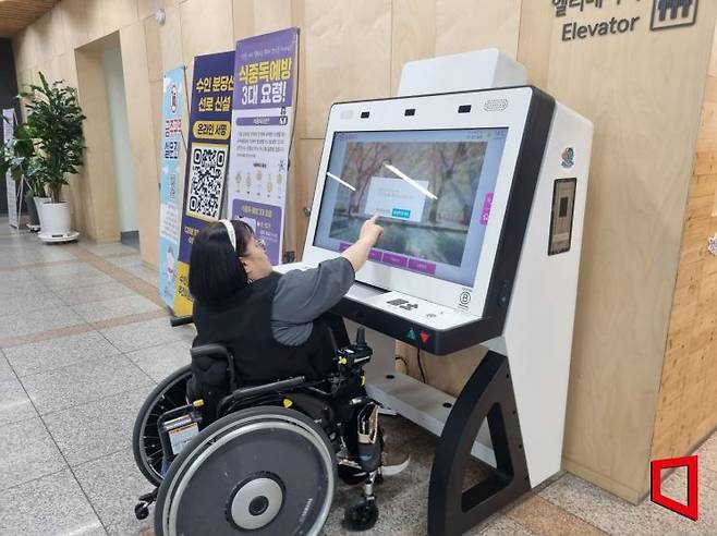 휠체어를 탄 시민이 서울 동대문구청 로비에 설치된 접근성 보장 키오스크를 이용하고 있다.[사진=심성아 기자]
