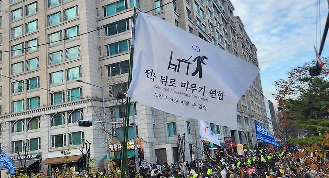 ‘전국 뒤로 미루기 연합’ 깃발이 7일 서울 여의도 국회 앞 집회 현장에서 휘날리고 있다. 온라인 커뮤니티 더쿠 사진 갈무리
