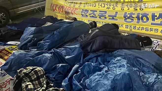 한화오션 하청 노조 조합원들이 천막 없는 농성장에서 침낭을 덮고 자고 있는 모습