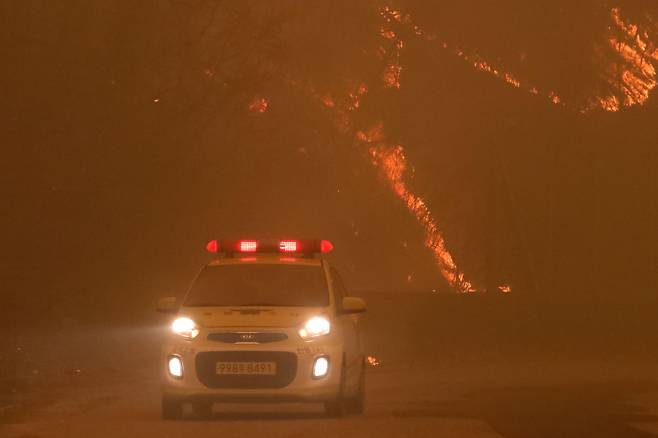 25일 오후 경북 안동시 길안면 백자리에 강풍이 불어 주변 산이 화염에 휩싸인 가운데 소방관계자들이 대피 명령이 내려진 마을 곳곳을 순찰하고 있다