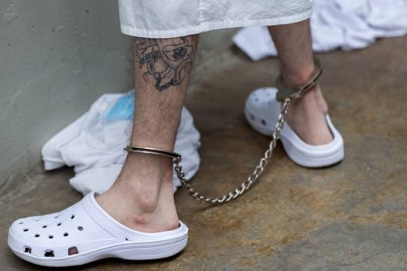 크리스티 놈(53) 미국 국토안보부 장관이 26일(현지시간) 엘살바도르에 있는 중남미 최대 규모 수감 시설 테러범수용센터(CECOT·세코트)를 방문한 가운데, 다리에 문신을 한 수감자가 족쇄를 차고 있다. 2025.3.26 AP 연합뉴스