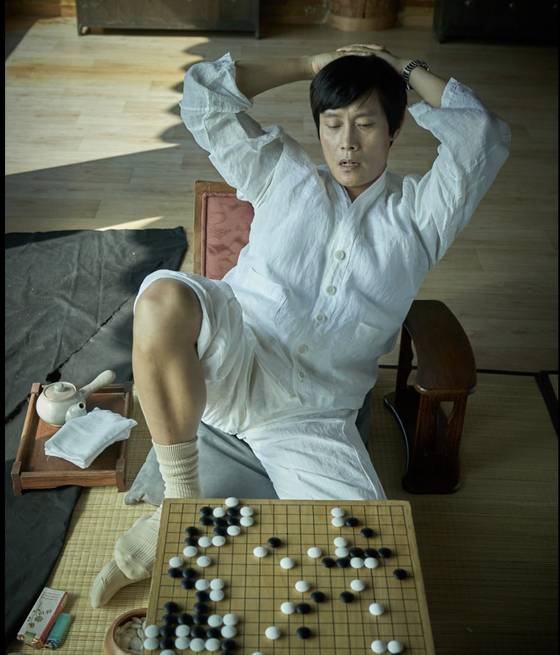 영화 '승부'에서 조훈현을 연기하는 이병헌. 조훈현은 한때 영화 속 장면처럼 흰 삼베옷을 즐겨 입었다. 소파에 길게 누운 자세로 바둑을 두는 자세도 유명하다. 사진 왼쪽 아래에 조훈현이 즐겨 피웠던 '장미' 담배가 보인다. 사진 바이포엠스튜디오