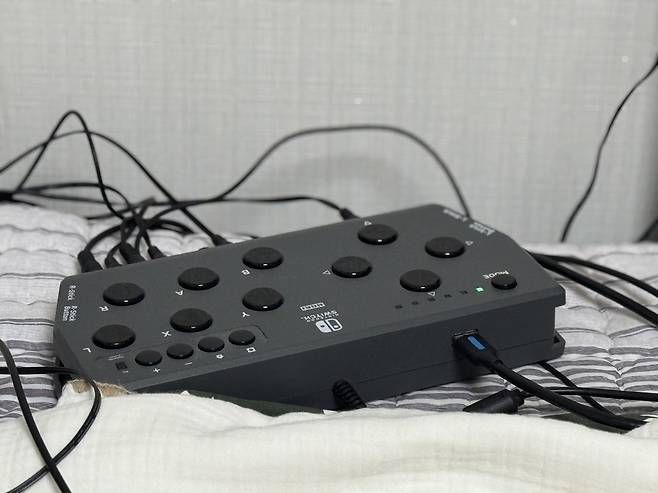 At the core of Jang Ik-seon’s gaming setup is the Flex Controller, a device that connects all his adaptive inputs into one seamless system. His chin joystick handles movement, his thumb presses ultra-sensitive buttons, and his toes operate additional switches — all wired through this central hub. While traditional controllers require two hands to use, the Flex Controller allows Jang to distribute controls across different parts of his body. (Moon Joon-hyun/The Korea Herald)