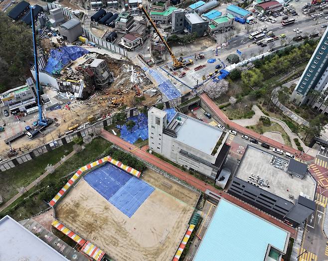16일 경기 광명시 일직동 신안산선 복선전철 5-2공구 붕괴 현장과 인근 초등학교 운동장에 깔린 균열 부위 방수포가 함께 보이고 있다. /뉴스1