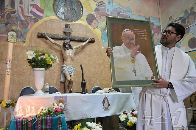 프란치스코 교황이 선종한 21일(현지시간) 아르헨티나 부에노스아이레스의 카쿠페 파리쉬에서 카리데스 신부가 고 프란치스코 교황의 초상화를 들고 있다. ⓒ AFP=뉴스1 ⓒ News1 포토공용 기자