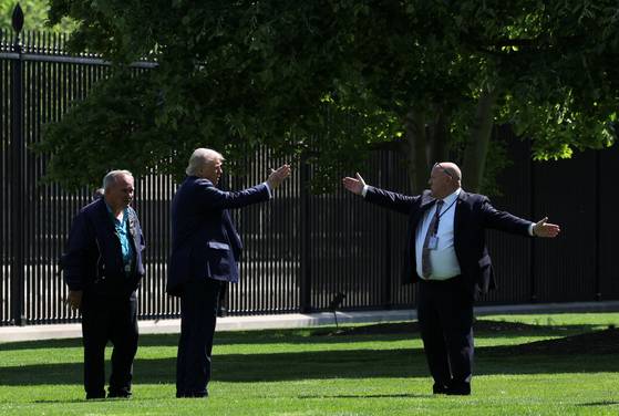 도널드 트럼프 미국 대통령(왼쪽에서 두 번째)이 지난 23일(현지시간) 백악관 북쪽 잔디에서 새로운 깃대 설치를 위해 백악관 직원들과 대화하고 있다. 한 남성이 양팔을 넓게 벌려 성조기의 크기를 표현하고 있다. 이들 두 깃대에 대형 성조기가 걸릴 예정이다. 로이터=연합뉴스