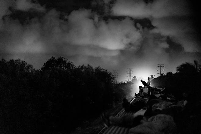 화물 열차의 지붕에 올라탄 이민자들 반대편에서 오는 다른 열차의 불빛이 나타나자 바라보고 있다. 2024.12. 멕시코 베르크루즈 주/ 사진가 양희석