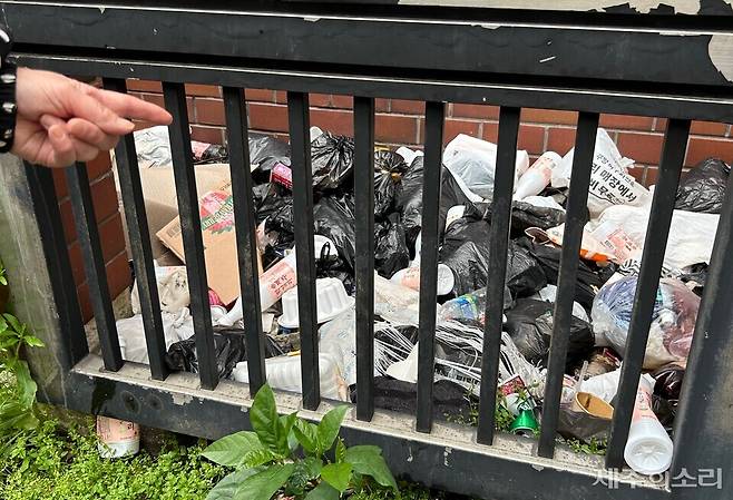 10일 오후 만난 상인 C씨가 건물과 울타리 사이 무단 투기된 쓰레기를 가리키고 있다. 내용물을 알 수 없는 검은 봉지와 막걸릿병, 담배꽁초들이 가득 쌓여있다. ⓒ제주의소리