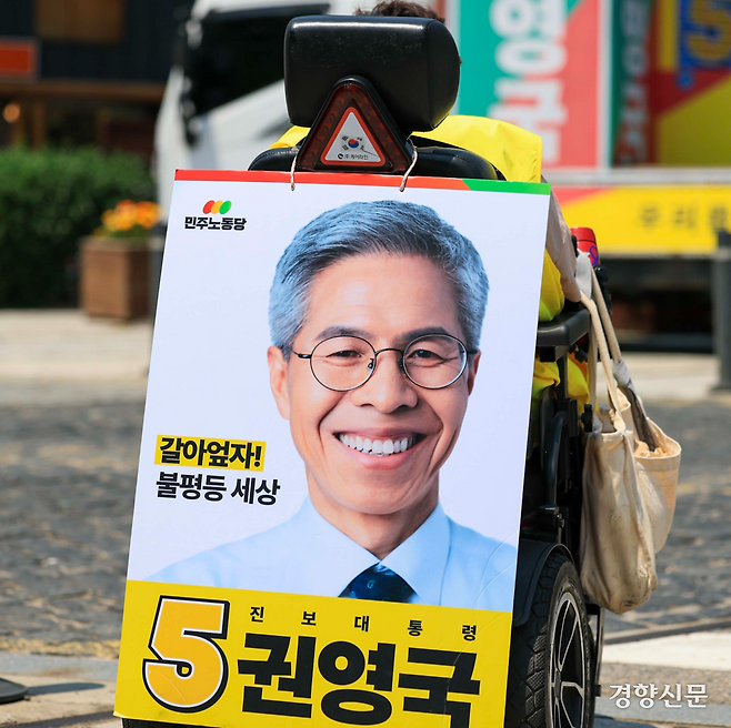 권영국 대선 캠프의 유세지원차량 앞에서 한 장애인 지지자가 휠체어 뒤에 권영국 후보 사진을 걸고 유세에 참여하고 있다. 이준헌 기자.