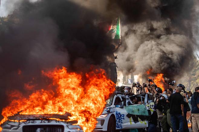8일 미국 캘리포니아 로스앤젤레스(LA)의 한 도로에 세워진 차들에서 화염과 짙은 연기가 솟아오르고 있다. 트럼프 행정부의 불법 이민자 단속에 항의하는 시위대가 차에 스프레이로 낙서를 한 뒤 방화한 것이다. 연기 사이로 멕시코 출신으로 추정되는 한 시민이 차 위에 올라타 멕시코 국기를 흔드는 모습이 보인다. 대규모 시위와 당국의 무력 진압으로 불거진 LA 소요 사태가 이날로 사흘째 이어졌다./AFP 연합뉴스