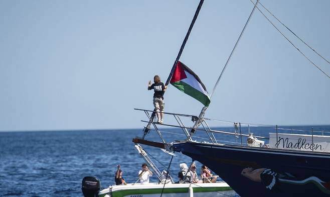지난 1일 기후변화 활동가 그레타 툰베리(사진 가운데)가 '자유선단연합' 소속 매들린호에 타서 배에 걸린 팔레스타인 국기 옆에 서 있다. 연합뉴스