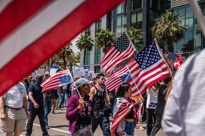 도널드 트럼프 미국 대통령의 79번째 생일이자 미 육군 창설 250주년 기념 열병식이 열린 14일(현지시각) 캘리포니아 샌디에이고에서 열린 ‘노 킹스’ 집회에서 시민들이 트럼프 행정부를 규탄하며 성조기를 들고 행진하고 있다. 샌디에이고/AFP 연합뉴스