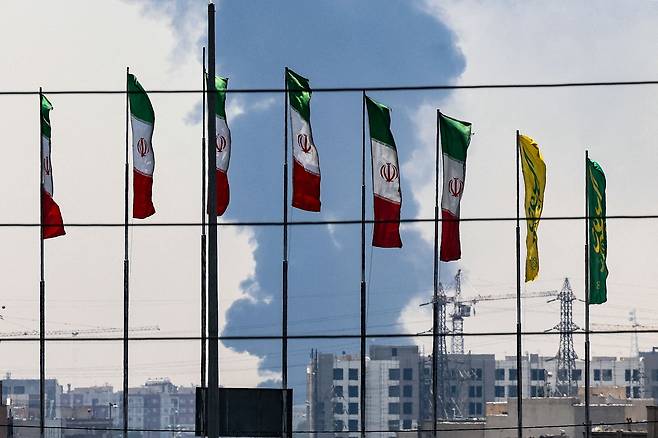 15일 이스라엘의 공습을 받은 테헤란 남부의 한 정유공장에서 짙은 연기와 불길이 피어오르는 가운데 다리를 따라 깃발이 펄럭이고 있다. /AFP 연합뉴스