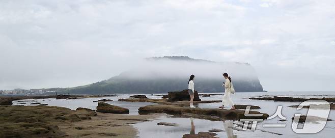 제주 서귀포시 성산읍 광치기해변에서 관광객들이 해무 낀 성산일출봉을 배경으로 사진을 찍고 있다. 2025.6.19/뉴스1 ⓒ News1 오현지 기자