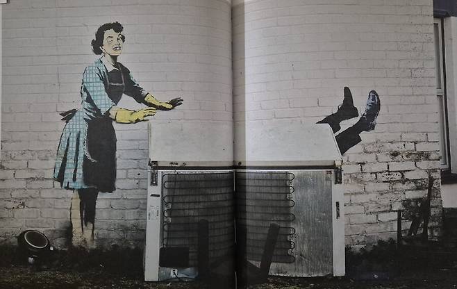 2023년 초 뱅크시가 영국 해변가 마을 뒷골목에 버려진 냉동고를 활용해 그린 ‘밸런타인데이 마스카라’. 1950년대 가정주부가 앞치마를 두르고 설거지 장갑을 낀 채 웃는데 멍들고 부은 눈과 빠지 앞니가 가정폭력을 암시한다. 남편은 냉동고에서 발만 삐져나온 것처럼 보이는데, 마땅한 대가를 치른 셈이다. 미술문화 제공