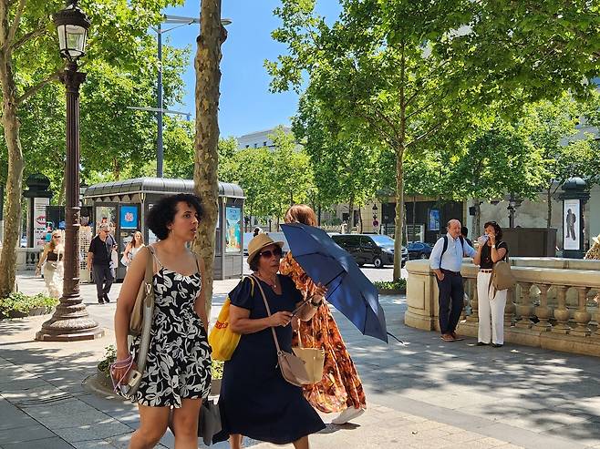 (파리=연합뉴스) 송진원 특파원 = 프랑스 파리 샹젤리제 거리에서 한 시민이 모자에 우산까지 챙겨들고 걸어가고 있다. san@yna.co.kr 2025.06.30.