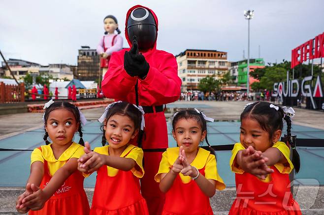 지난 30일(현지시간) 태국 방콩 시청 광장에서 열린 '오징어 게임 3' 홍보 행사에서 어린이들이 오징어게임 진행요원 복장을 착용한 사람과 기념촬영을 하고 있다. ⓒ 로이터=뉴스1