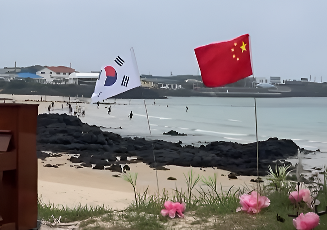 제주 우도에서 전동차를 타고 관광하던 중 한 시민이 오성홍기를 발견했다는 영상이 스레드 게시물을 통해 확산됐다. 깃발은 바닥에 고정돼 있었고, 피아노·연꽃 모형과 함께 설치돼 있었다. 누리꾼들은 “나라 뺏겨도 되냐”는 등 강한 반응을 보였다. (사진=스레드)