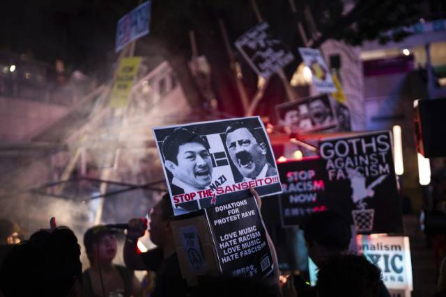 13일 일본 도쿄 신주쿠에서 ‘외국인 규제’를 주장하는 참정당에 반대하는 항의 집회가 열린 가운데 집회 참가자가 참정당 가미야 소헤이 대표와 히틀러 사진을 붙인 피켓을 들고 있다./AP 연합뉴스