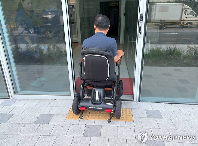 건물 내부로 들어가고 있는 이범재 대표 (서울=연합뉴스) 최혜정 인턴기자 = 지난 8일 이범재 유니버설하우징협동조합 대표가 휠체어를 타고 유니버설디자인하우스-장안 건물 내부로 들어가고 있다. 2025.7.18