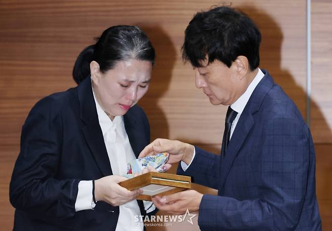 故 오요안나의 어머니 장연미씨가 15일 서울 마포구 상암동 MBC에서 진행된 유족측 기자회견에 앞서 안형준 MBC 사장으로부터 고인의 명예사원증을 받은 뒤 눈물을 흘리고 있다. /2025.10.15 /사진=이동훈 photoguy@