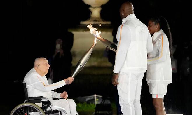 2024년 7월 27일 파리 올림픽 개막식 당시 1948년 런던 올림픽 금메달리스트 샤를 코스테(왼쪽)가 프랑스 스포츠 영웅이자 성화 최종 점화자인 마리 호세 페렉(오른쪽)과 테디 리네르(가운데)에게 성화봉을 건네고 있다. AP연합뉴스