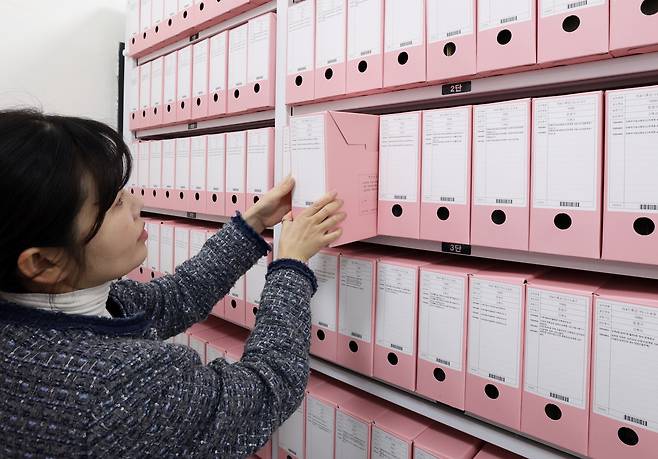 황외정 주무관이 분홍색 서류철을 빼내어 정리하고 있는 모습이다.서류 보관 캐비넷에 분홍색 서류철들이 가득 채워져 있다.