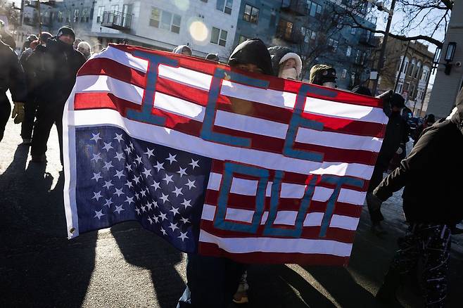 현지시간 24일 미 연방 경찰관이 37세의 알렉스 프레티를 총격으로 살해한 후 미네아폴리스 남부에서 행진하는 사람들 사이에서 한 사람이 거꾸로 된 미국 국기를 들고 있다. AP=연합뉴스