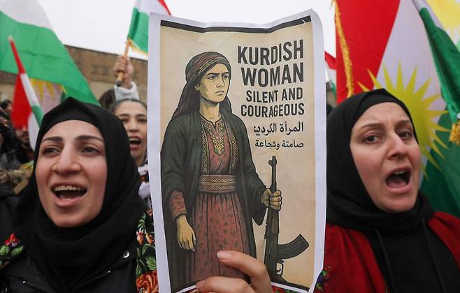 지난달 23일 이라크 북부 에르빌에서 쿠르드족 여성들이 무장한 쿠르드 여성의 모습을 그린 포스터와 쿠르드 깃발을 들고 시위를 벌이고 있다. 시리아 정부군 연계 무장 민병대가 쿠르드족 여전사를 살해한 뒤 잘라낸 머리채를 보여주는 것으로 추정되는 영상이 공개된 것에 대한 항의다. AFP=연합뉴스