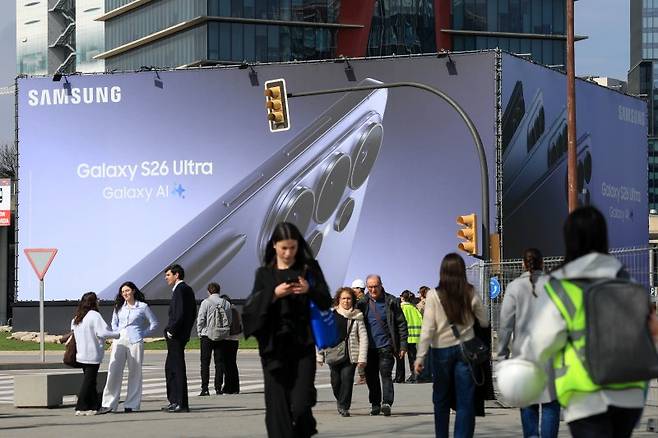 2일(현지시간) 스페인 바르셀로나에서 개막한 세계 최대 이동통신 전시회 '모바일월드콩그레스(MWC) 2026' 전시장 인근에 설치된 삼성전자 갤럭시 S26 울트라 광고판 앞을 사람들이 지나가고 있다. 올해 MWC는 SK텔레콤, KT, LG유플러스, 삼성전자, SK하이닉스, LG전자, 벤처·스타트업 등 한국 기업 182개사가 참가했다.