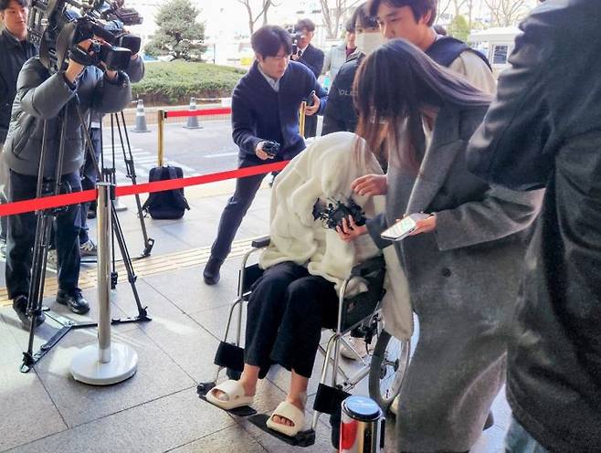 약에 취한 상태로 포르쉐 SUV 차량을 몰고 반포대교를 달리다 한강 둔치로 추락한 운전자 A씨가 지난달 27일 서울 마포구 서부지방법원에서 열린 구속 전 피의자 심문(영장실질심사)에 옷으로 얼굴을 가리고 휠체어를 탄 채 출석하고 있다. 연합뉴스