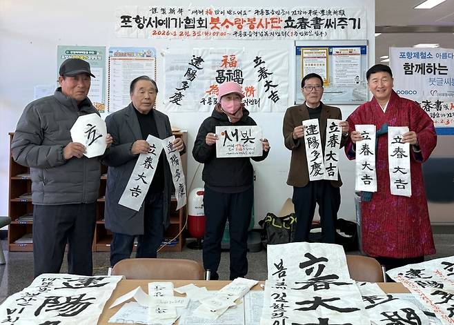 ▲ 강성태 서예가가 설맞이 붓글씨 봉사 현장에서 시민들과 함께 새해 덕담 글귀를 들고 기념촬영을 하고 있다. 강성태씨 제공