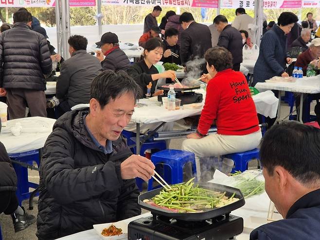 지난 13일 미삼 직거래 장터 내 마련된 미삼 체험장에서 한 시민이 미나리와 삼겹살을 불판에 올려놓고 구우면서 환하게 웃고 있다. 이승엽기자