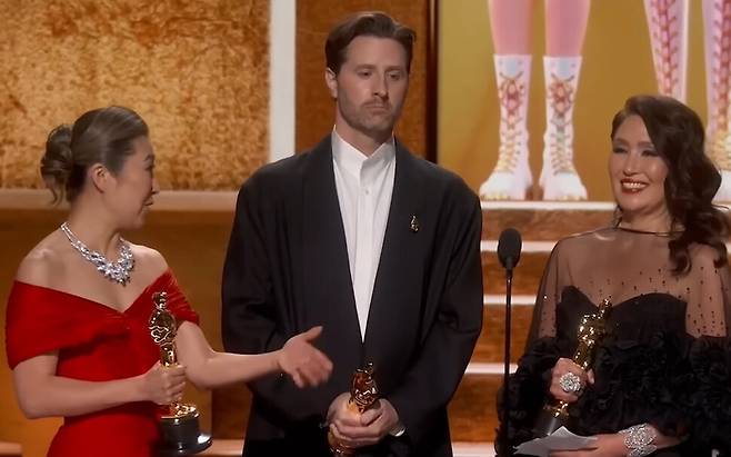 제98회 아카데미 시상식에서 장편 애니메이션상을 수상한 매기 강 감독과 공동 연출자 크리스 아펠한스, 제작자 미셸 웡이 무대에 서 있다. 미셀 웡(제일 오른쪽)이 수상 소감을 말하는 도중 노래가 흘러나와 당황하고 있는 장면. 에이비시 뉴스(ABC News) 유튜브 갈무리