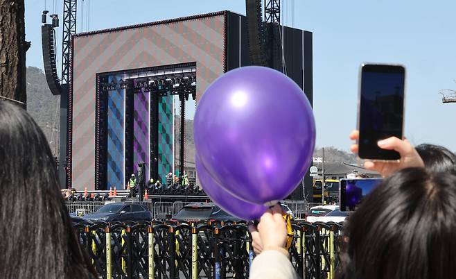 그룹 방탄소년단(BTS)의 컴백 공연을 이틀 앞둔 19일 서울 종로구 광화문 광장에서 BTS를 상징하는 보라색 풍선을 든 시민들이 무대 설치작업을 보고 있다./연합뉴스